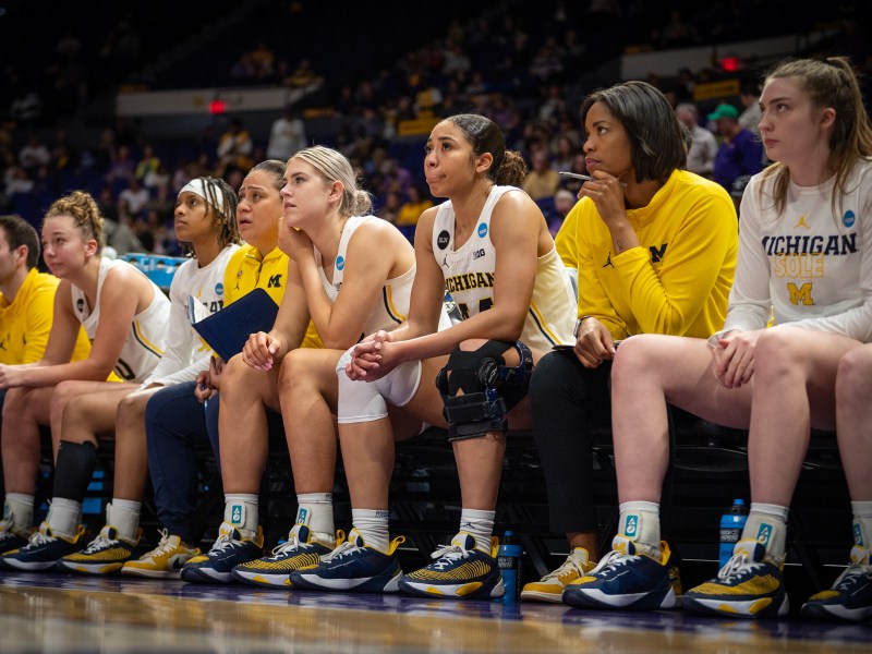 A photo of the Michigan bench. Coaches and players watch the court intently.