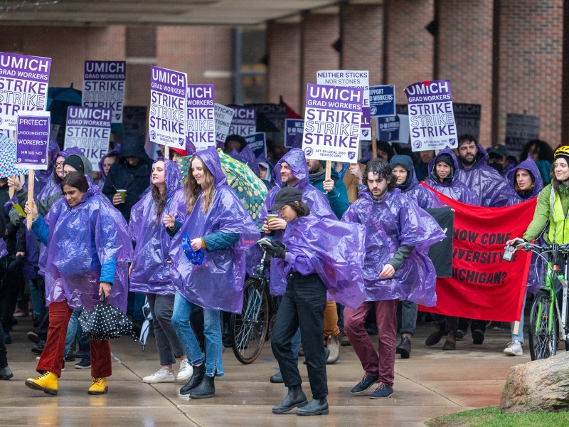 GEO walks through campus in purple ponchos holding signs that read "UMICH GRAD WORKERS STRIKE, STRIKE, STRIKE"