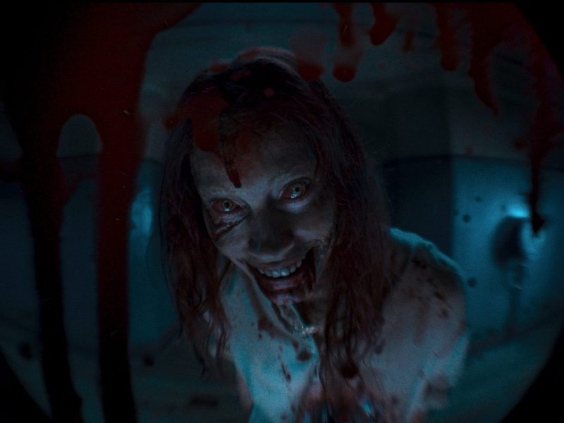Image of a woman from Evil Dead Rises smiling creepily while covered in blood.