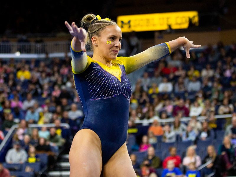 Abby Heiskell looks focused as she performs her floor routine. Her arms are raised on either side of her as the crowd watches in the background at Crisler Center.