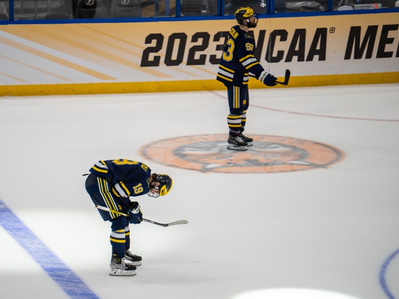 Adam Fantilli bends over as another Michigan player skates away in defeat at the Frozen Four.