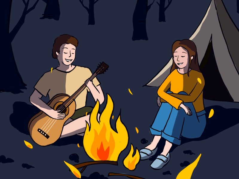 Man and woman sitting together around a campfire. The man is playing the guitar.