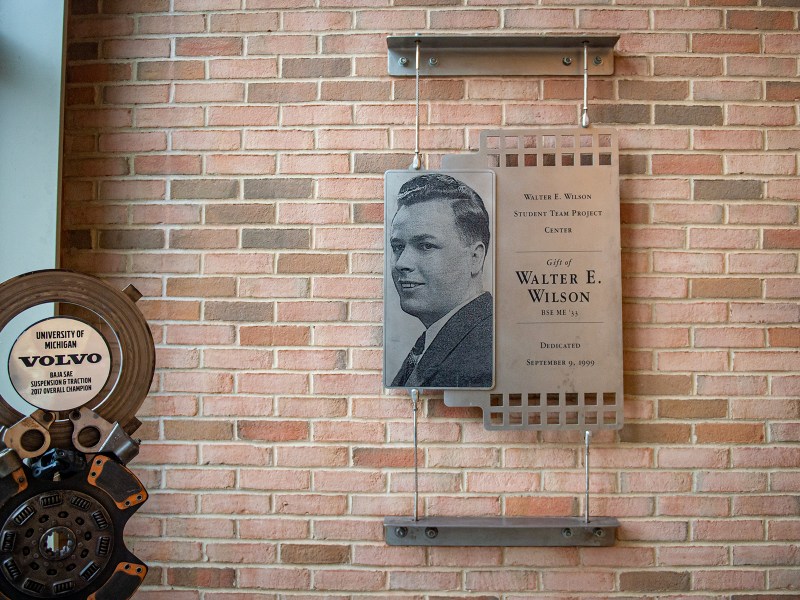 A silver plaque in the center of the image displays a picture of a young Walter E. Wilson, and there is a Volvo Baja SAE project car trophy in the bottom left corner.