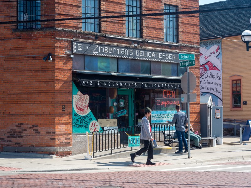 The Zingermans storefront is pictured with two pedestrians walking out front of it.