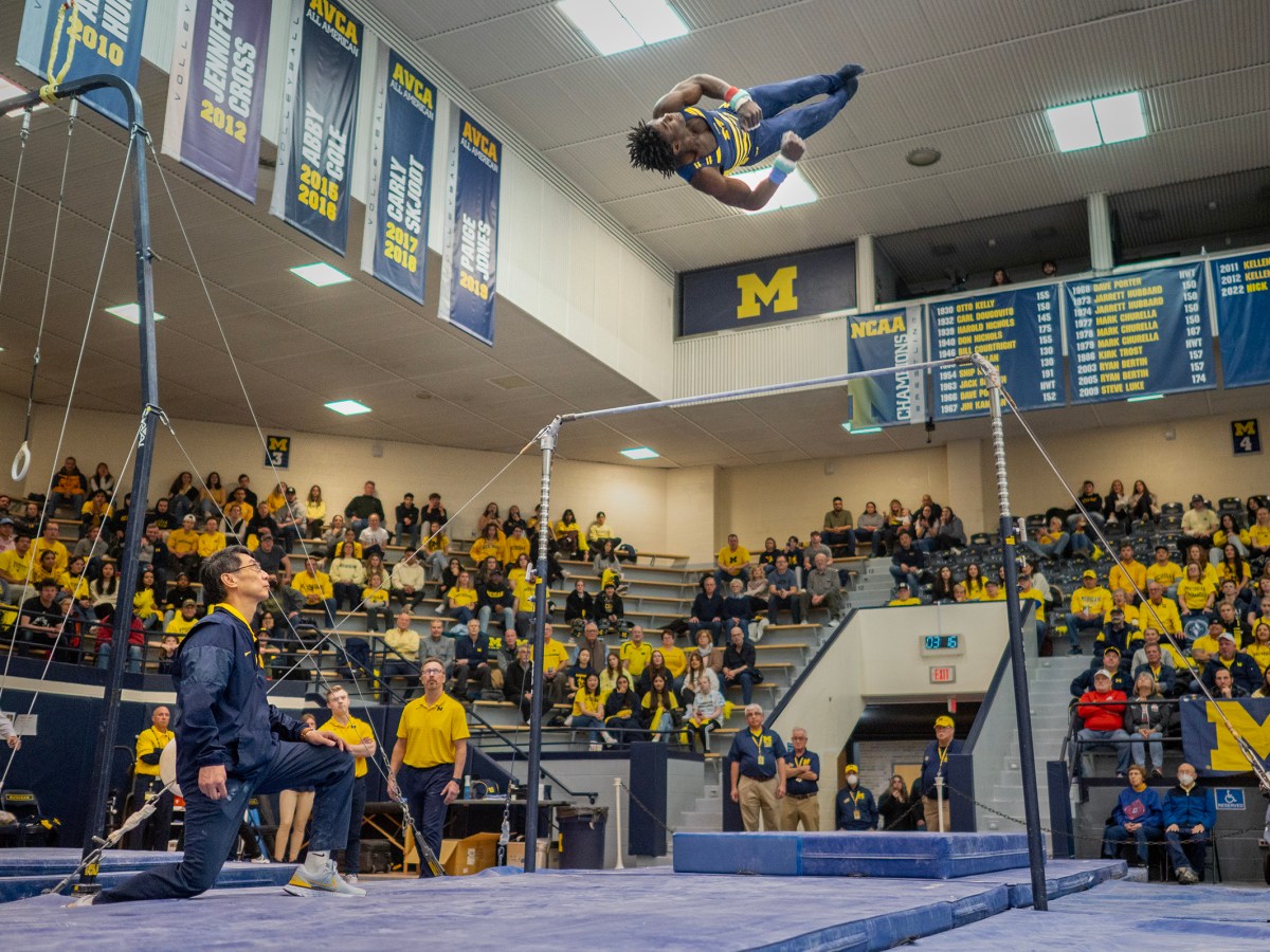 Fred Richard flies in the air during his dismount from the bar. His coach watches on below.