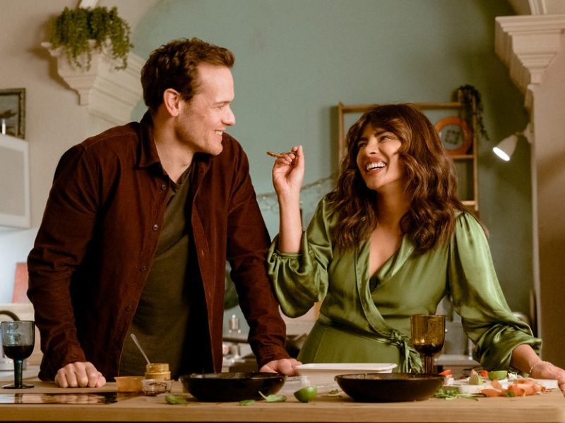 Priyanka Chopra smiling widely in a green dress cooking with Sam Heughan.