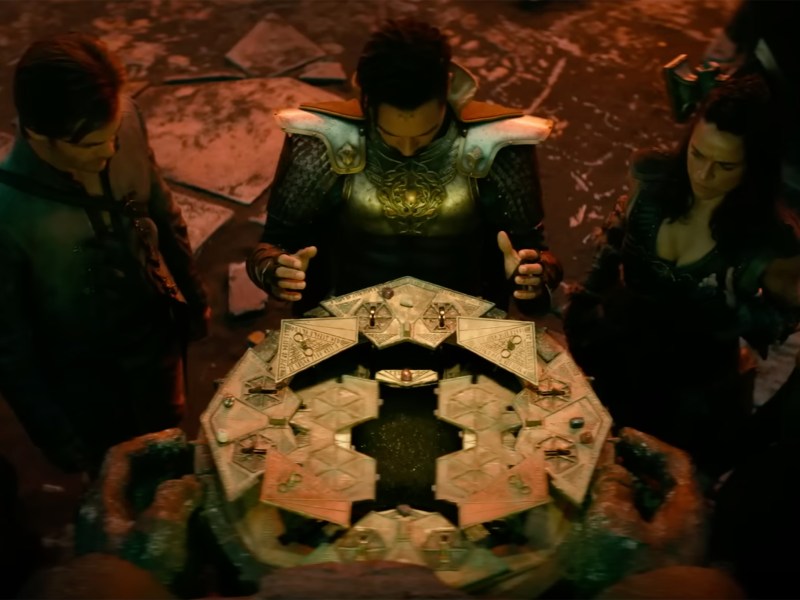 Four characters in medieval fantasy outfits surround an unfolding magical container.
