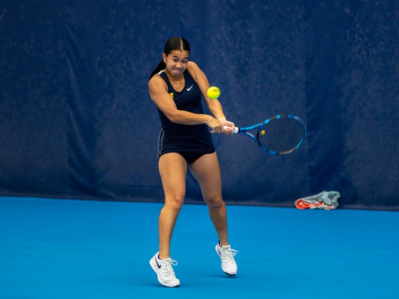Tennis player, Andrea Cerdan, holds her racquet with both hands as she swings to hit the ball.