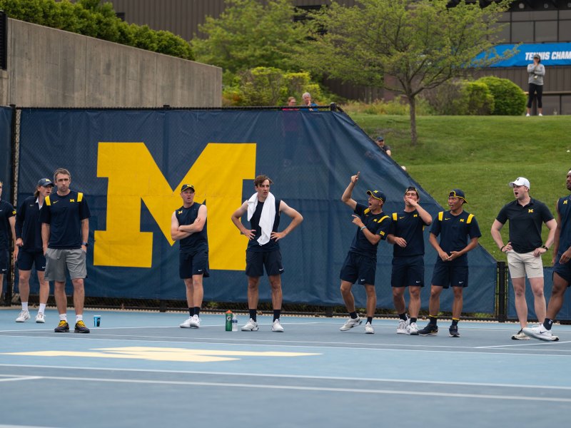 The men's tennis team lines up. The Block M is in the background.