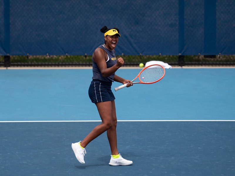 Jaedan Brown celebrates, pumping a fist in the air and holding her racket in the other hand.