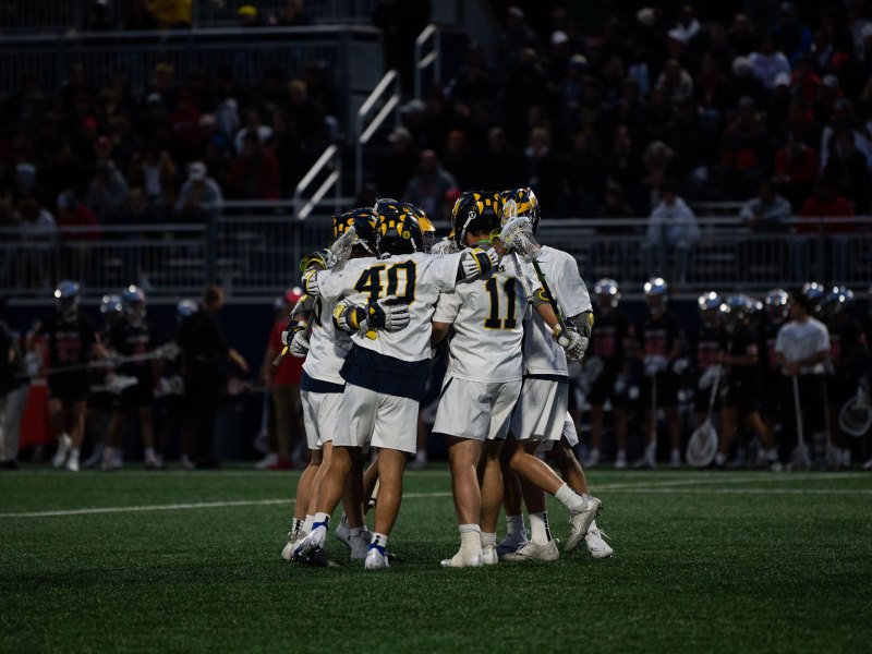 The Michigan Men's Lacrosse team celebrates a goal. The Ohio State sideline stands in the background.