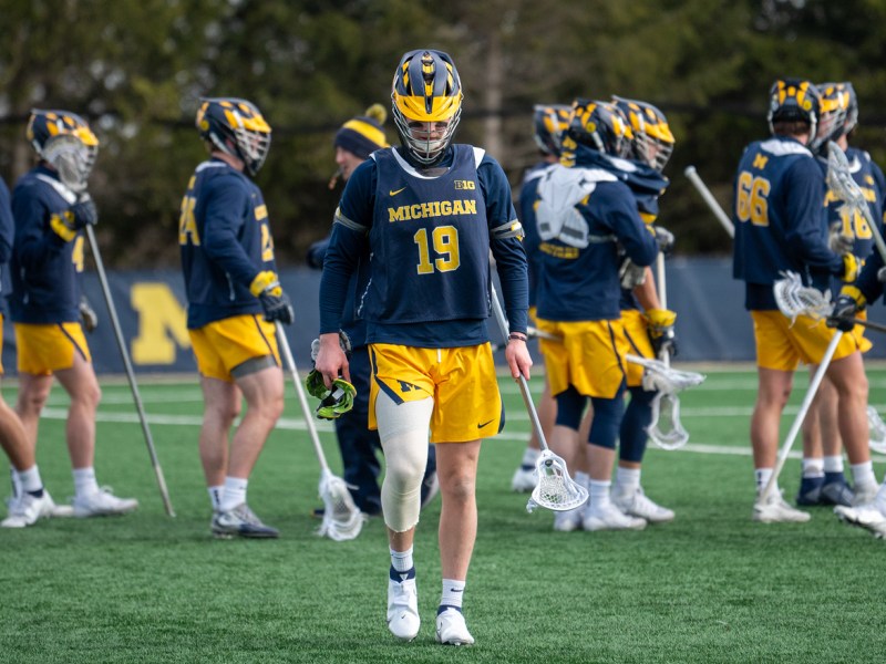 A lacrosse player walks towards the bench with his head down. The rest of his team stands behind him.