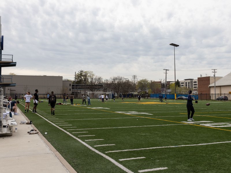Students play football and spike ball and other activities on the green of Elbel field with blue cloudy skies in the background.
