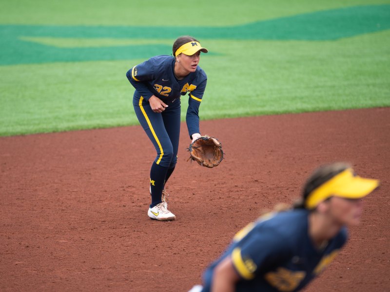 Ella McVey is crouched with her glove open. Her teammate stands in front and to the right.