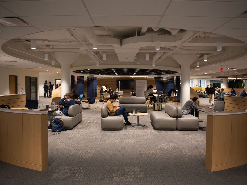 Students study and lounge in the Clark Commons. There are couches in the center of the image and students standing up are gathered in small groups.