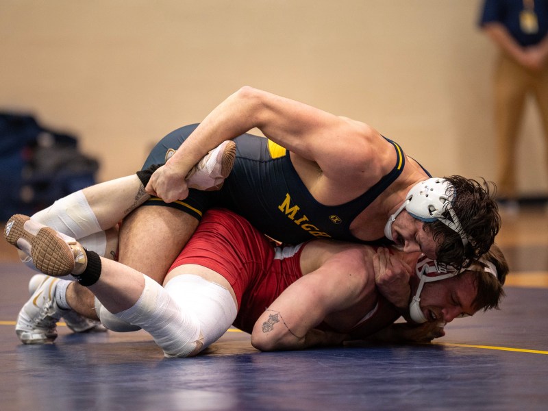 A Michigan wrestler crushes his opponent below him on the mat.