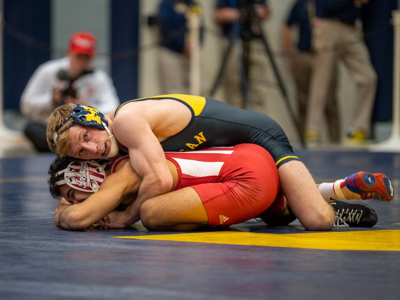 A Michigan wrestler holds his opponent in a tight embrace below him on the mat.