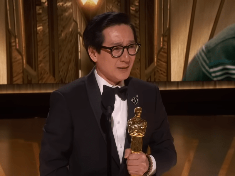 Actor Ke Huy Quan on stage at the 2023 Oscars, holding an Academy Award
